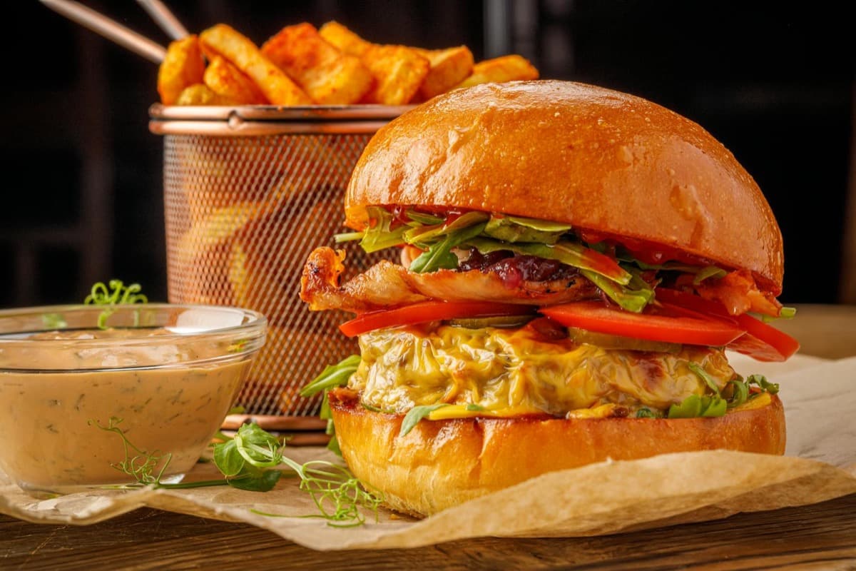 A stacked gourmet burger on a brioche bun with fries and dipping sauce (16:9)