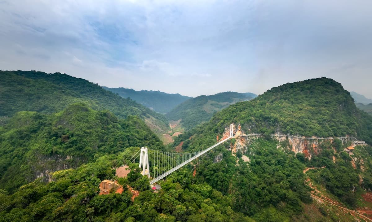 A long pedestrian suspension bridge spanning a deep forested mountain valley (16:9)