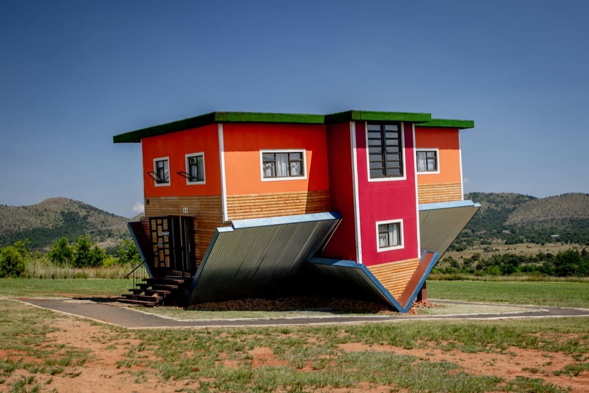 A brightly colored upside-down building attraction on a grassy lawn (16:9)