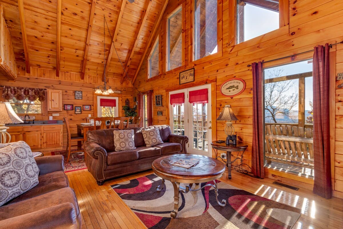 Open-plan main living room with leather sofas, round coffee table, vaulted pine ceiling, and kitchen visible