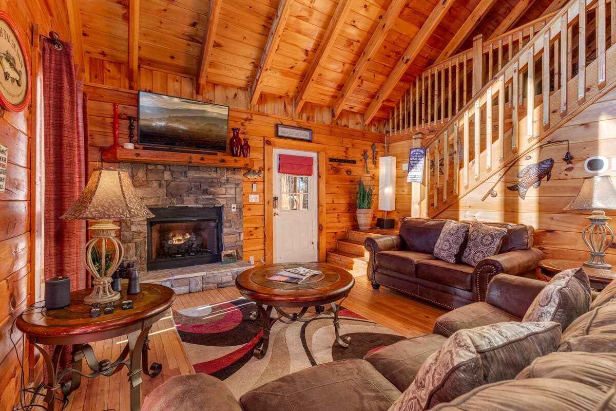 Living room with stone fireplace, TV above mantle, leather sofas, and stairs leading up to loft game room