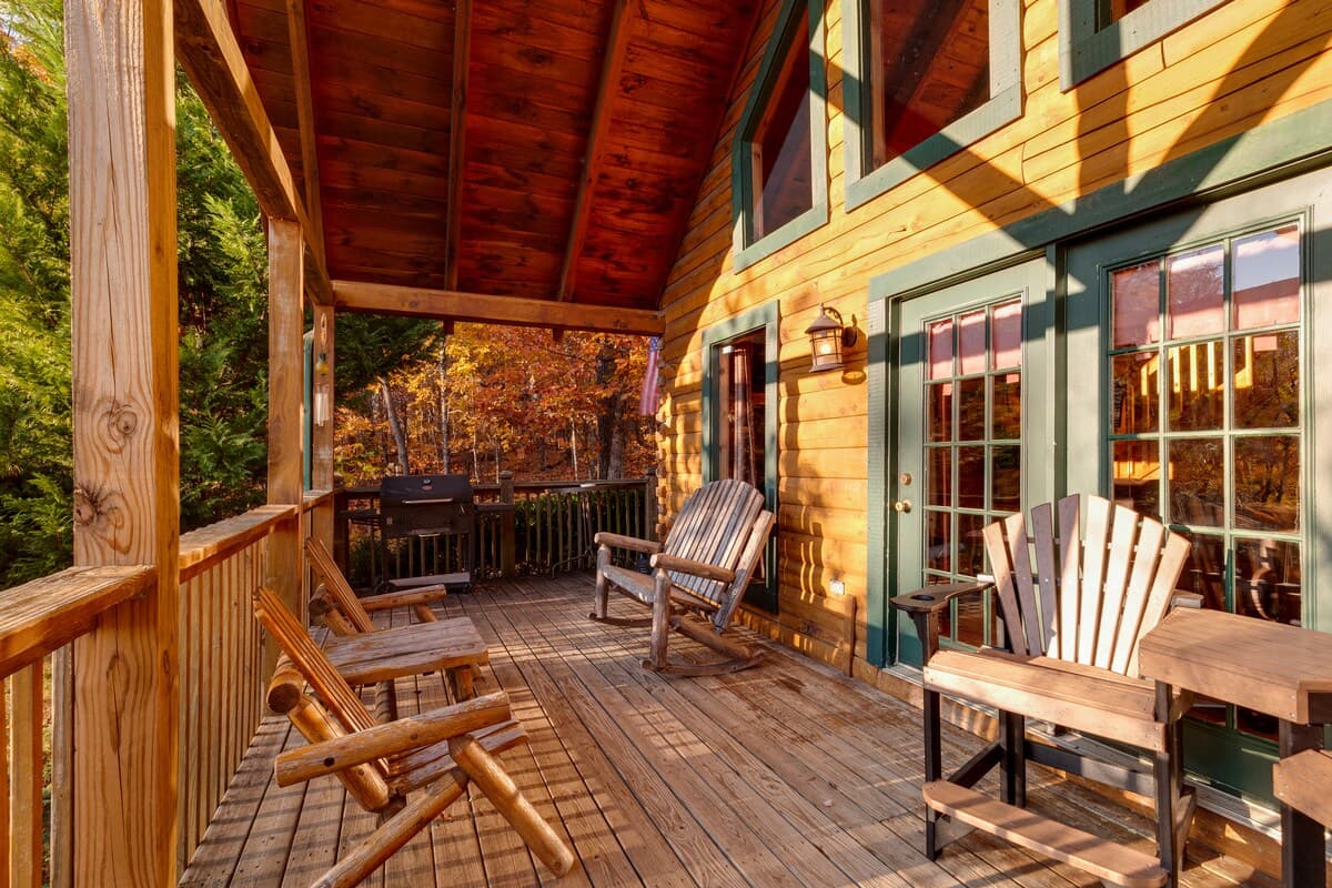 Covered wraparound porch with Adirondack chairs, log rocker, green trim, and warm autumn light