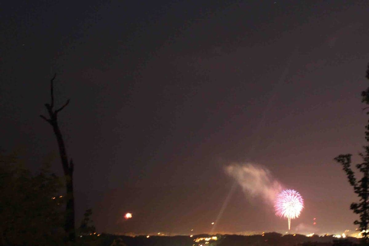 Fireworks bursting over Pigeon Forge at night viewed from the cabin with tree silhouettes