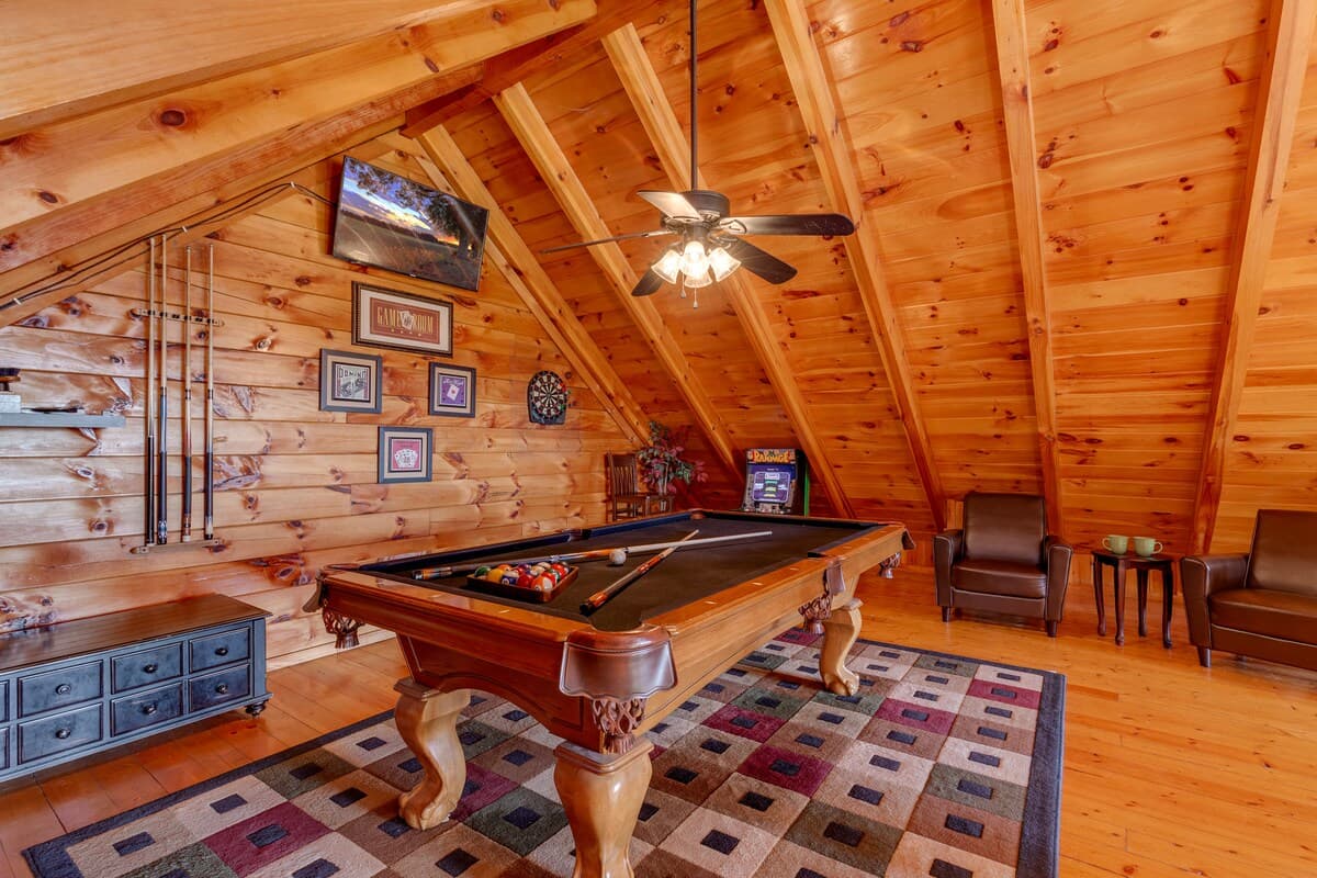 Loft game room wide view with pool table, leather armchair, patterned rug, and vaulted pine ceiling