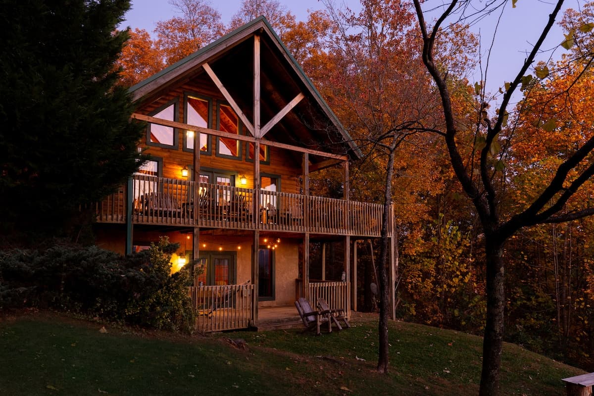 Cabin exterior at dusk in autumn with warm string lights on lower deck and fall foliage