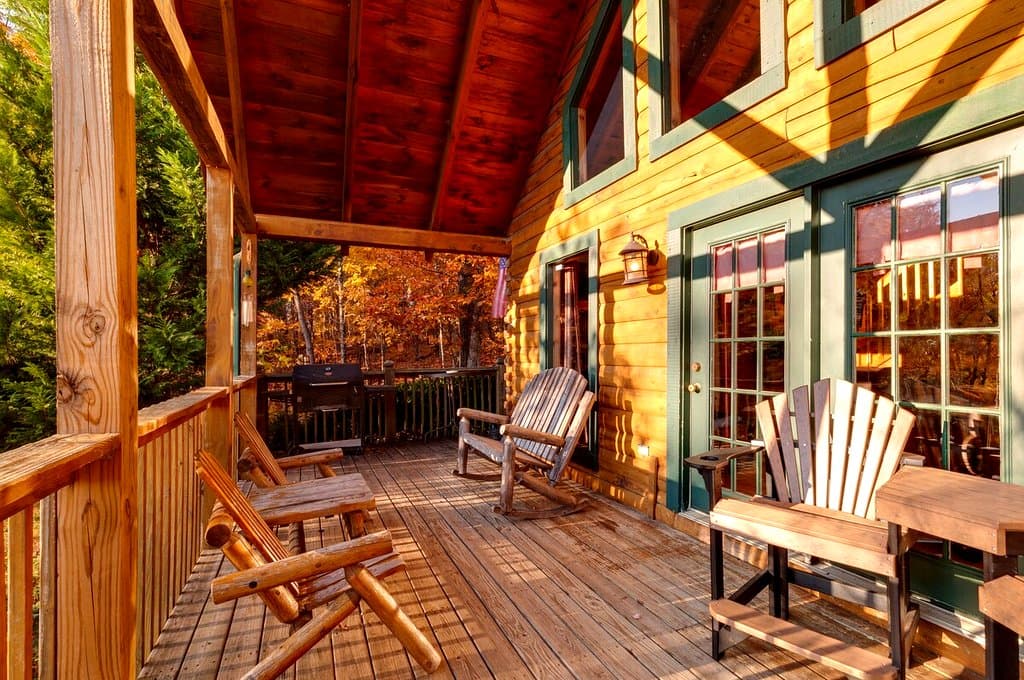 Rocking chairs along a covered deck with autumn trees beyond