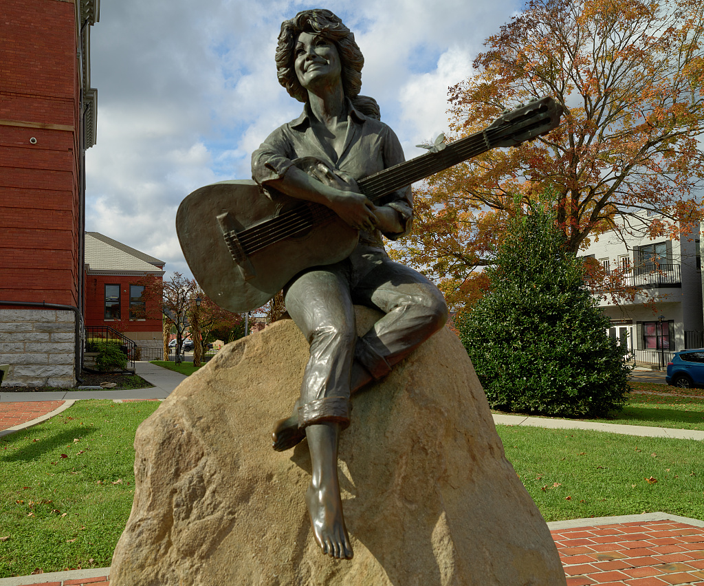 Bronze statue of Dolly Parton holding a guitar outside the Sevier County Courthouse, with autumn trees behind it
