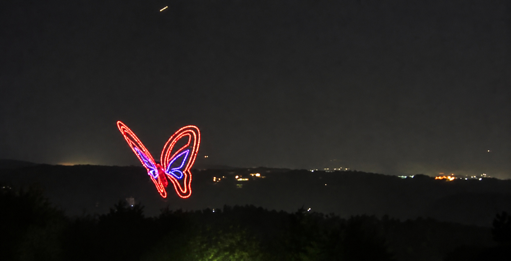 A red and purple butterfly formed by Dollywood's drone show above the dark ridge, photographed from our cabin deck