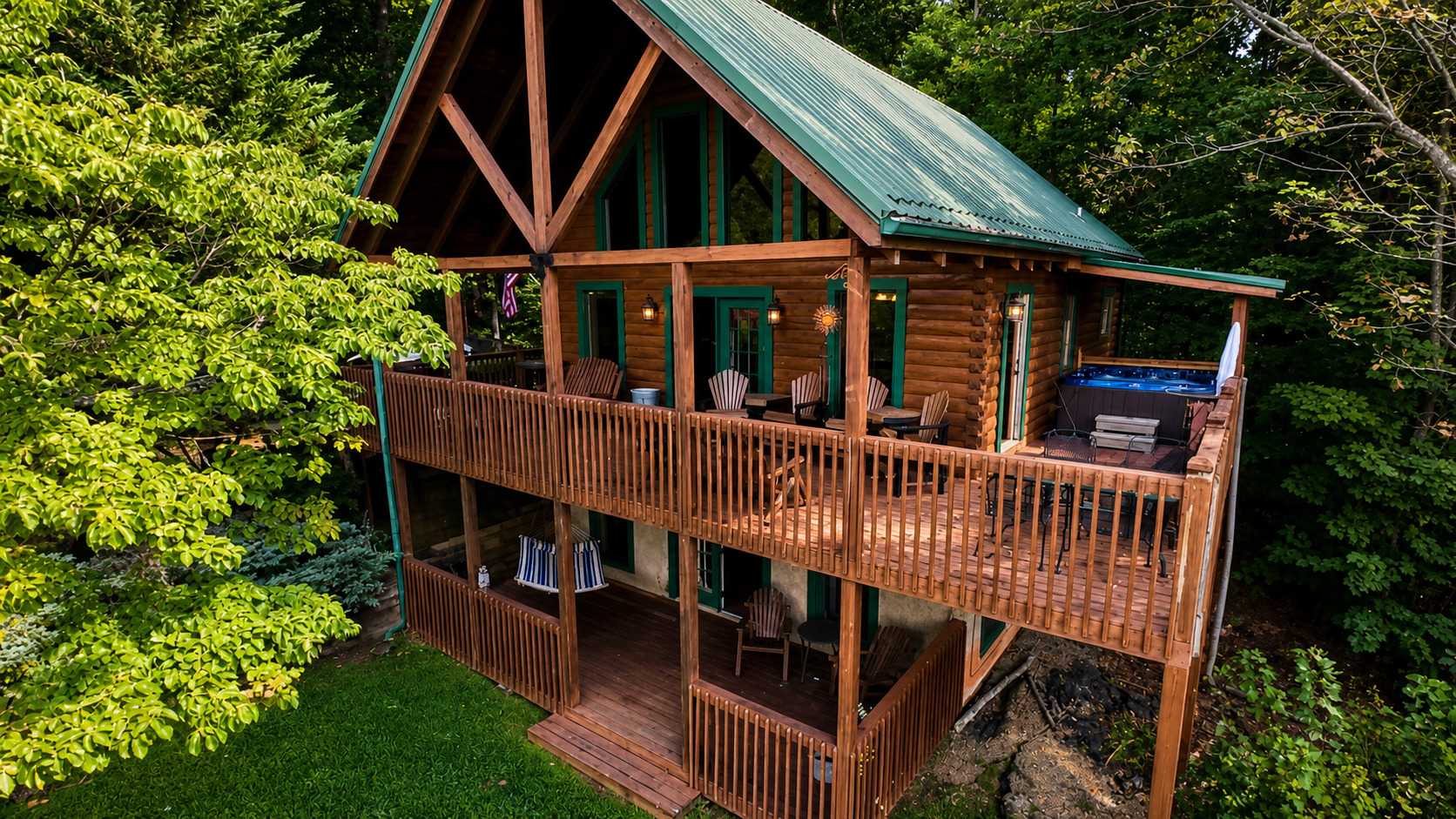 Thistle Britches log cabin with a green roof and two wooden decks surrounded by leafy trees